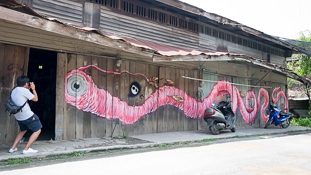 Community-based tourism in an urban environment. Tourist appreciating urban artwork in Ban Pong, Ratchaburi Province, Thailand. 