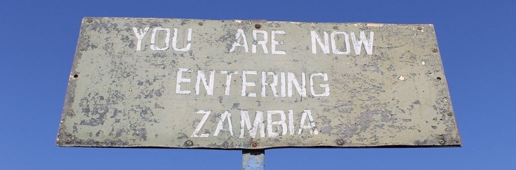 "You are now entering Zambia" road sign. Photo by scooterenglasias (CC0) via Pixabay. https://pixabay.com/photos/zambia-roadsign-africa-2646990/