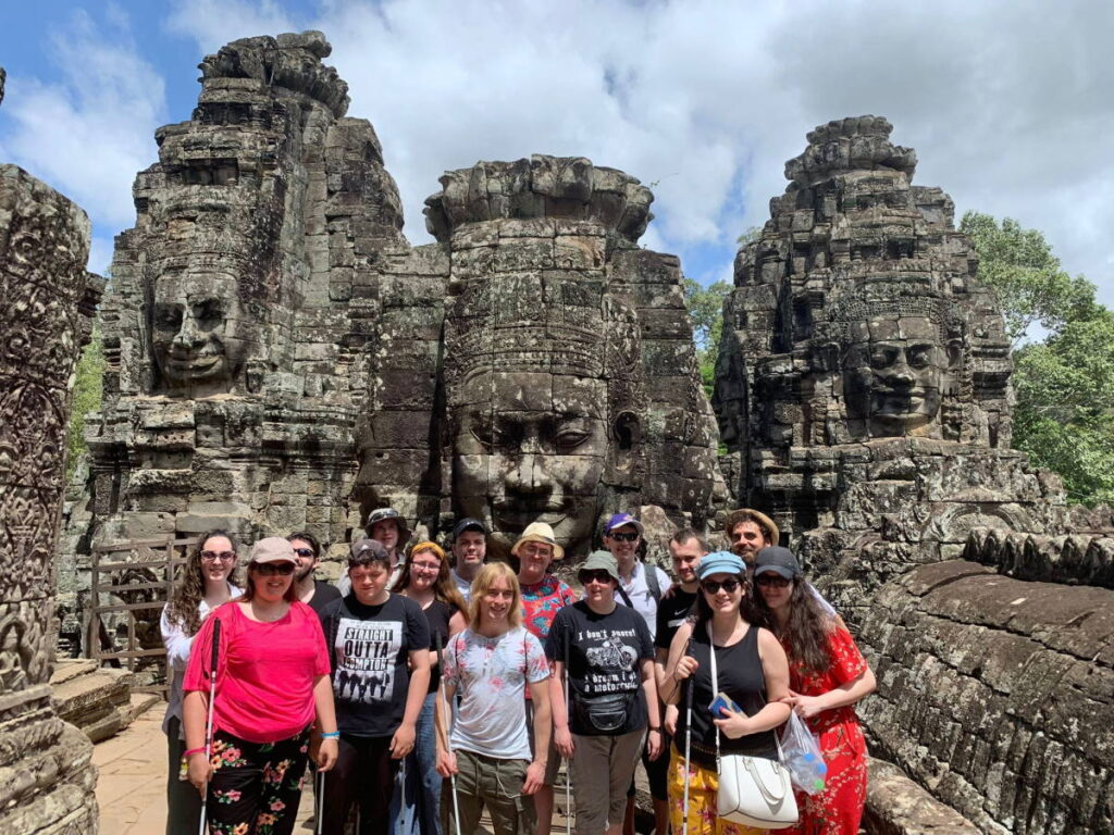 Group of 15 visually-impaired travellers posing for a photo in front of the Bayon, Angkor, Cambodia